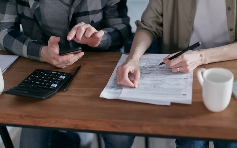 Dos personas revisando formas de impuestos con calculadora